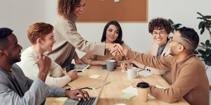 female loans consultant shaking hands with the team leader sitting beside his smiling colleagues