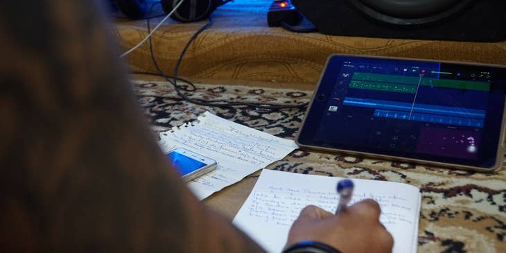 Lyricist writing lyrics on a notebook and pen and using a tablet playing a recording