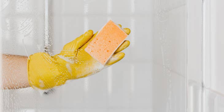 Maid wearing gloves cleaning a shower cabin glass