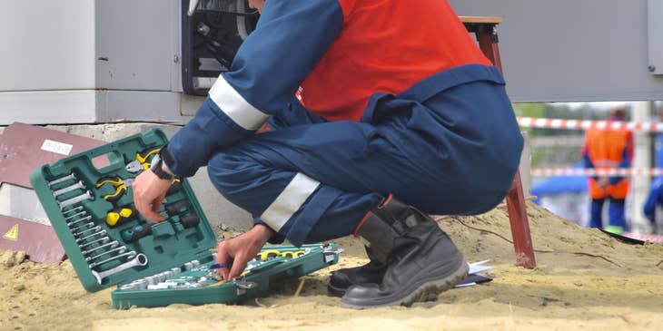 Maintenance Engineer crouching on the ground while rummaging through his toolbox for a scheduled on-site repair