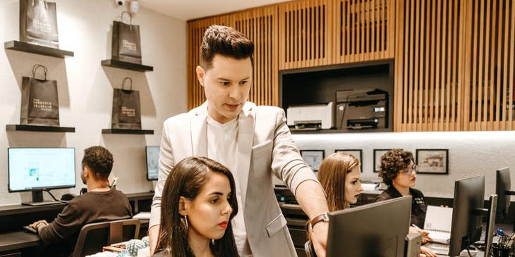 Manager talking to one of his staff who is sitting in front of her desktop