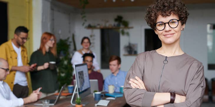 Managing partner wearing eyeglasses and standing inside the conference room while the rest of the team on the background is on break