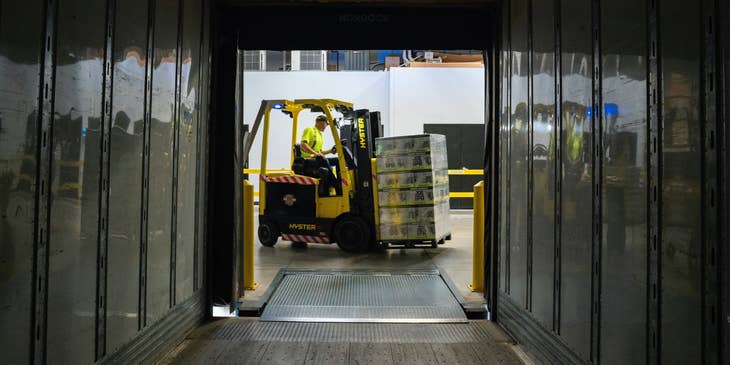 A material handler driving a forklift and about to transfer packages from the truck to the designated area inside the warehouse.