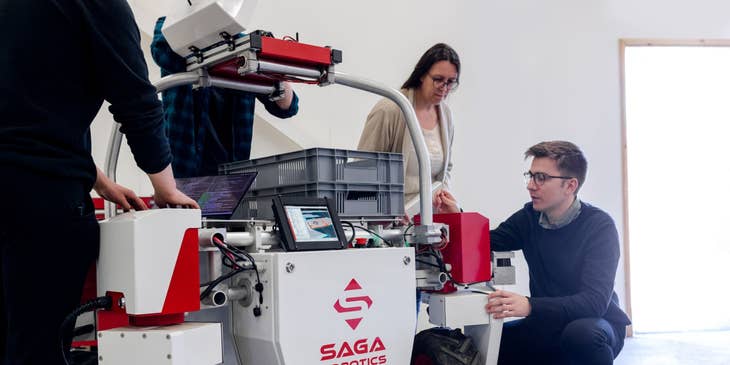 Mechatronics engineer checking an agricultural robot prior for further development while the rest of his team looks on