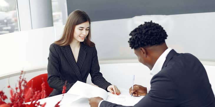 female mortgage processor smiling and looking over a client signing papers on the table