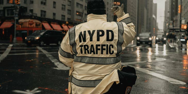 A patrol officer directing traffic on a rainy day in the middle of a busy street.