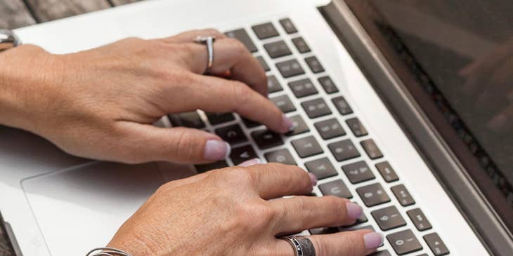 A payroll director typing on a laptop next to an open notebook.