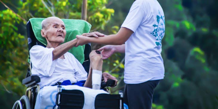 Personal care assistant holds the hand of elder patient as mobility support.
