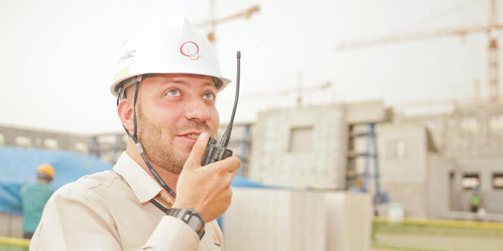 Petroleum engineer holding a wireless handset and wearing a hard hat while coordinating the location of extraction to his colleague.