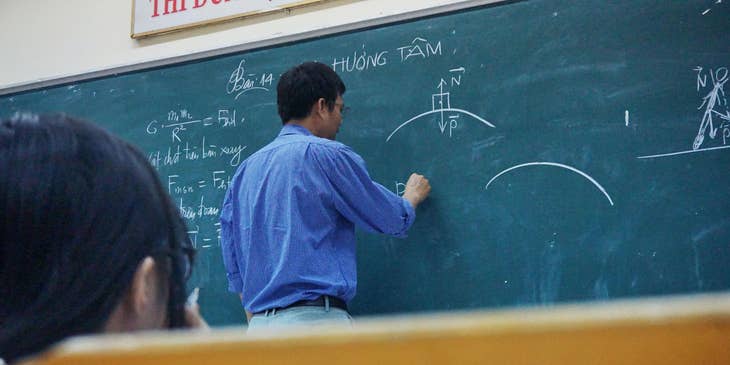 Physics teacher explaining the formula to students while writing on the board.