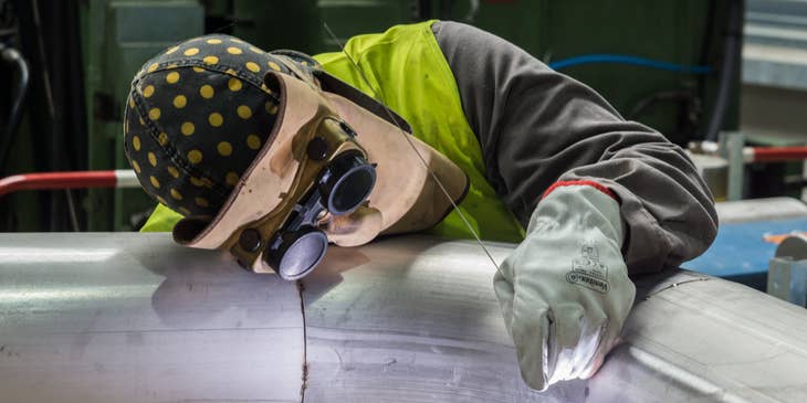 welder in full protective gear welding a pipe