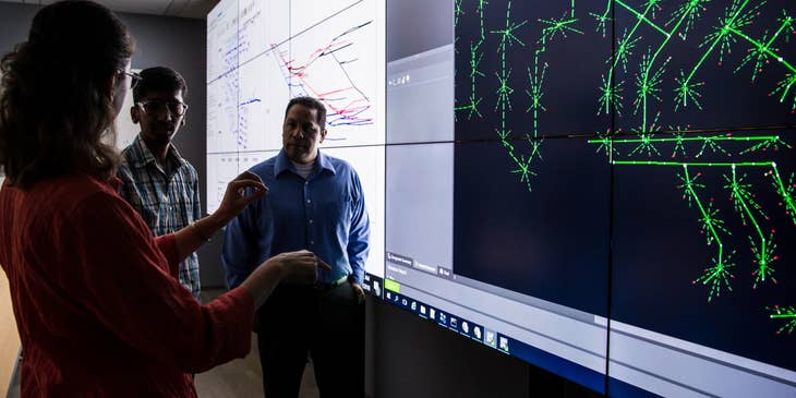 Planning engineer presenting an updated project timeline to the lead engineers while standing in front of the projected screen