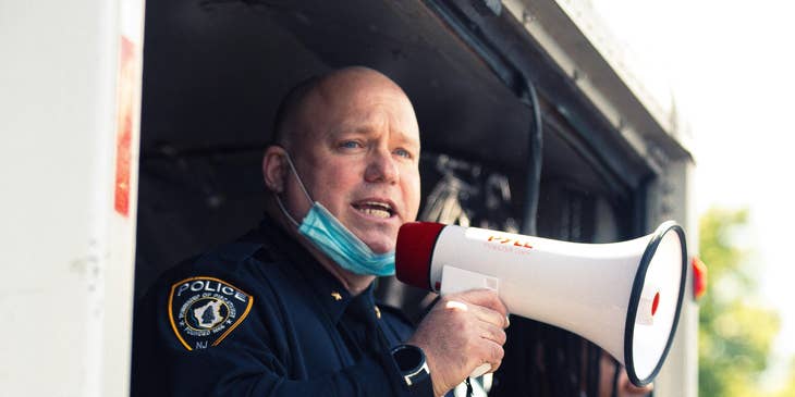 A police sergeant on duty talking through a megaphone and assisting his subordinates during a protest.