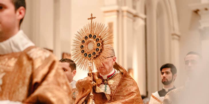 a priest holding the golden cross during the opening of the Mass