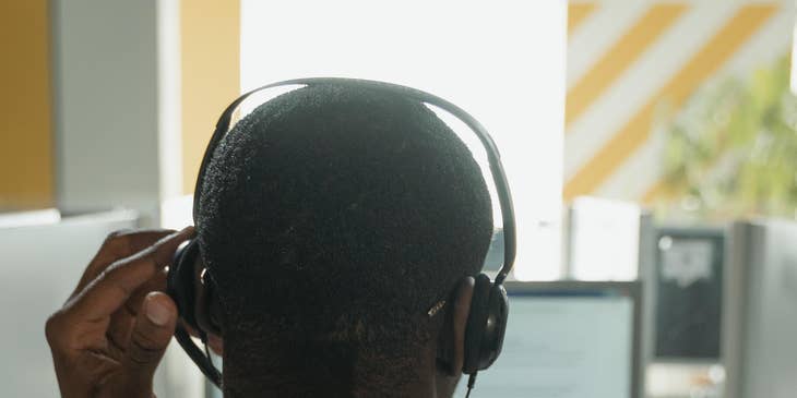 A progressive claims adjuster trainee in an office setting with a headset on his ears in front of a computer.