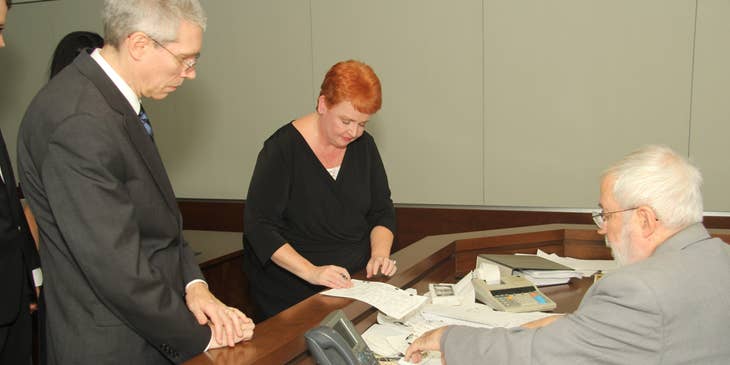 A male prosecutor with a female client in front of a judge in a courtroom signing documents.