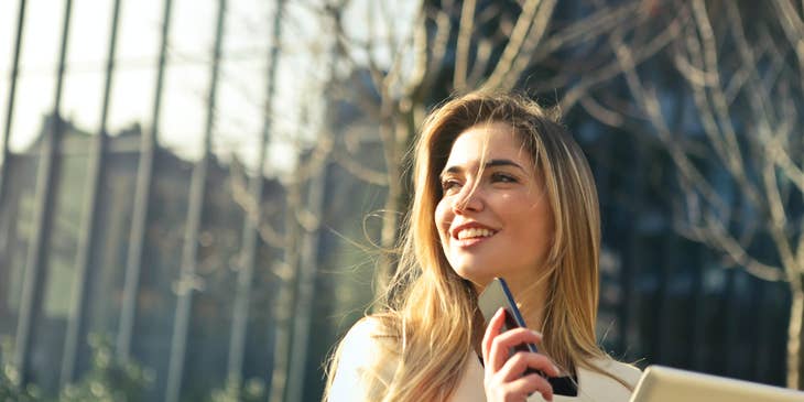 Woman holding a smartphone and Ipad in front of a house.