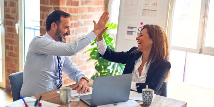 two Relationship Executives sitting in the office while smiling and giving high-five