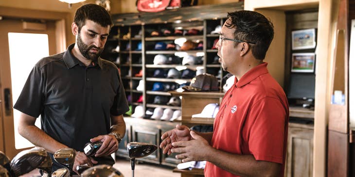 A sales representative selling golf clubs to a customer.