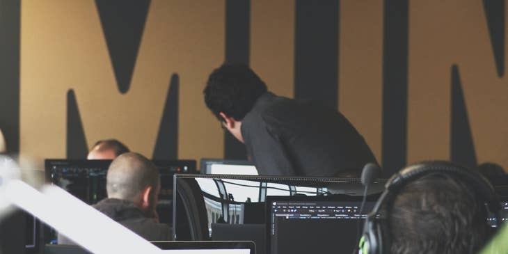 Scrum master standing beside his colleague's workstation and providing guidance