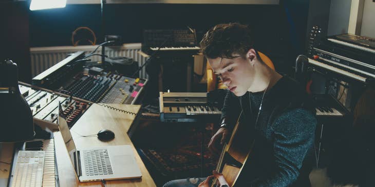 songwriter working in a studio with a guitar and laptop