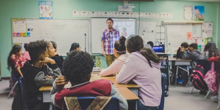 A Spanish Teacher in front of students in a classroom teaching about Spanish Culture.