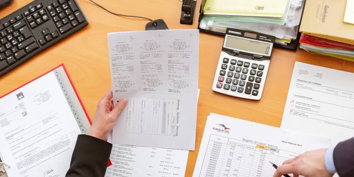 photo of one person holding a paper on his left hand and pen on the other hand while the other person is pointing out something on the desk