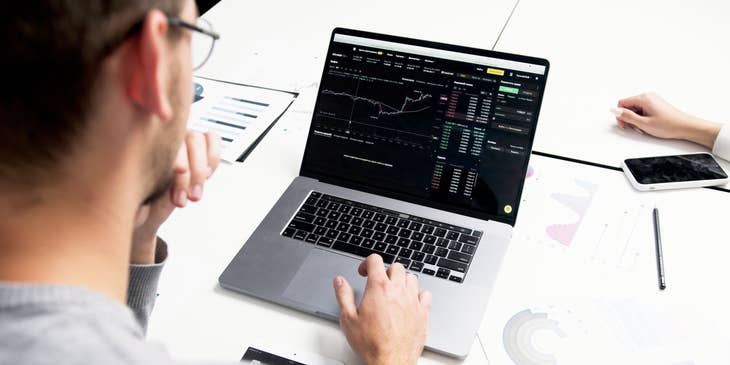 Trader wearing eyeglasses while looking at a real-time report on his laptop