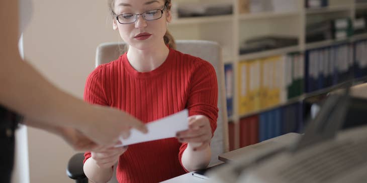 Veterinary Office Manager wearing eyeglasses and receiving a piece of paper from a pet owner