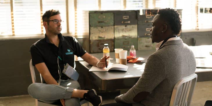 male Victim Advocate wearing glasses and sitting on the table while holding a pen and having a dialogue with his client